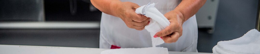 Wäschereimitarbeiter/in faltet Wäsche