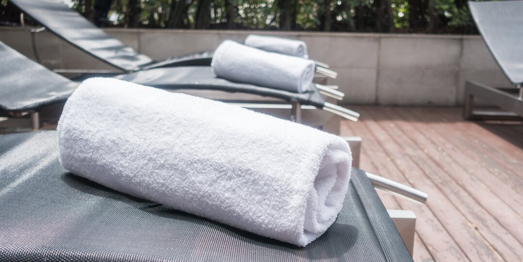 Dussmann Wäscheservice für Wellnessbereiche, der weiche, saubere und hygienische Wäsche liefert, die auf die Bedürfnisse von Spas, Wellnesszentren und Hotels zugeschnitten ist, wobei strenge Hygiene- und Qualitätsprotokolle eingehalten werden. | © <a href="https://www.freepik.com/free-photo/white-towels-deck-chairs_952848.htm">Image by mrsiraphol on Freepik</a>